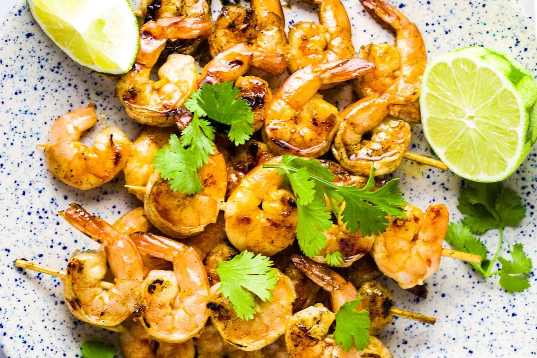 Shrimp skewers on a platter with a garnish of lime wedges and cilantro