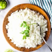 A large wooden bowl full of rice, garnished with a sprig of cilantro