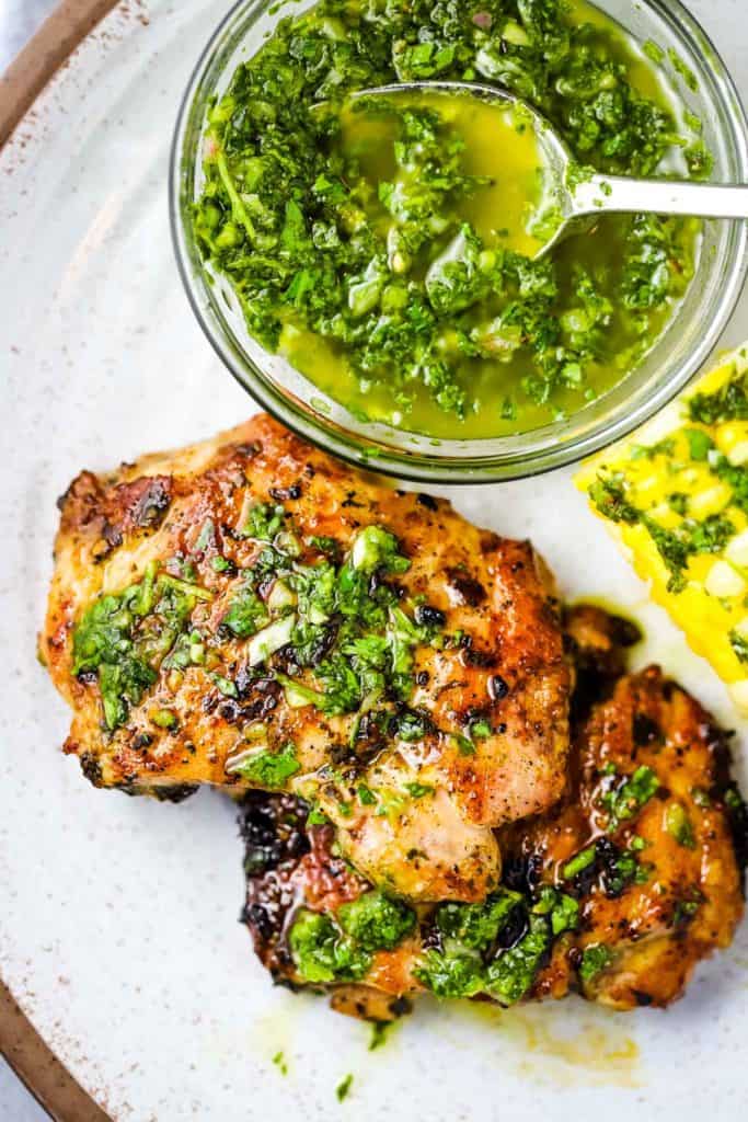 Pieces of chicken on a plate with a bowl of chimichurri