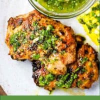 Pieces of chicken on a plate with a bowl of chimichurri