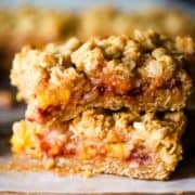 Two peach and raspberry oatmeal bars stacked on top of parchment paper