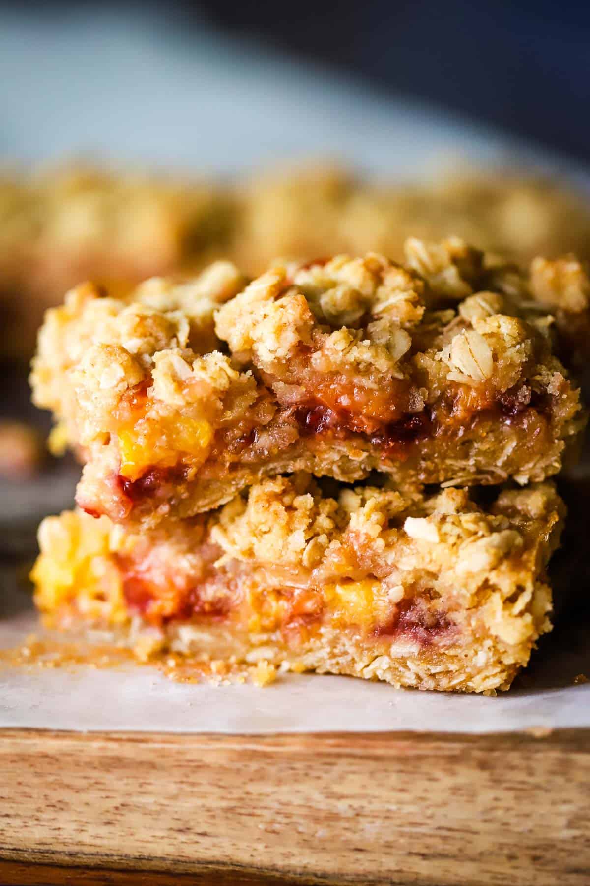 Two peach and raspberry oatmeal bars stacked on top of parchment paper