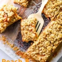 Peach and raspberry oatmeal bars on parchment with a spatula picking one up with text overlay