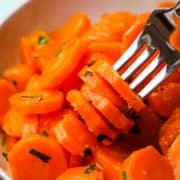 A bowl of sauteed carrot coins with a few coins speared on a fork.