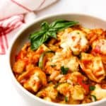 A serving of baked tortellini in a bowl garnished with basil leaves.