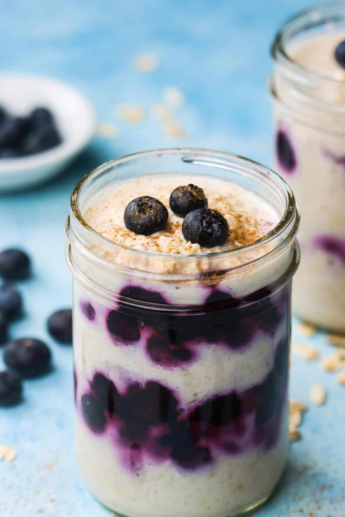 A jar of blueberry overnight oats topped with fresh berries and sprinkled with cinnamon.