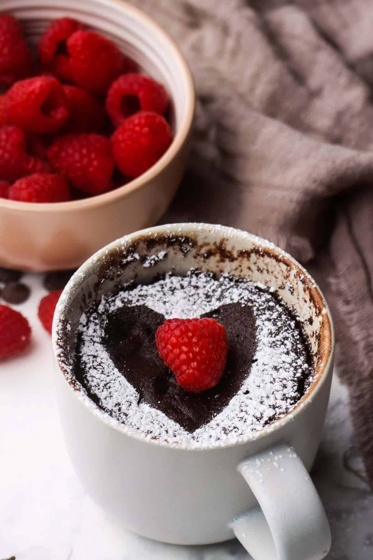 Chocolate raspberry cake in a mug with a fresh raspberry on top.