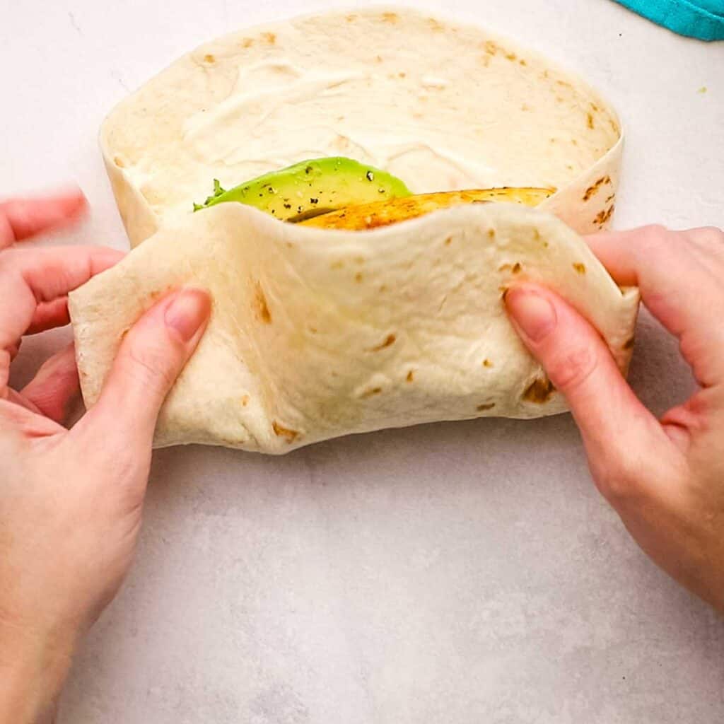 Pressing one side of the tortilla to the center with the filling.