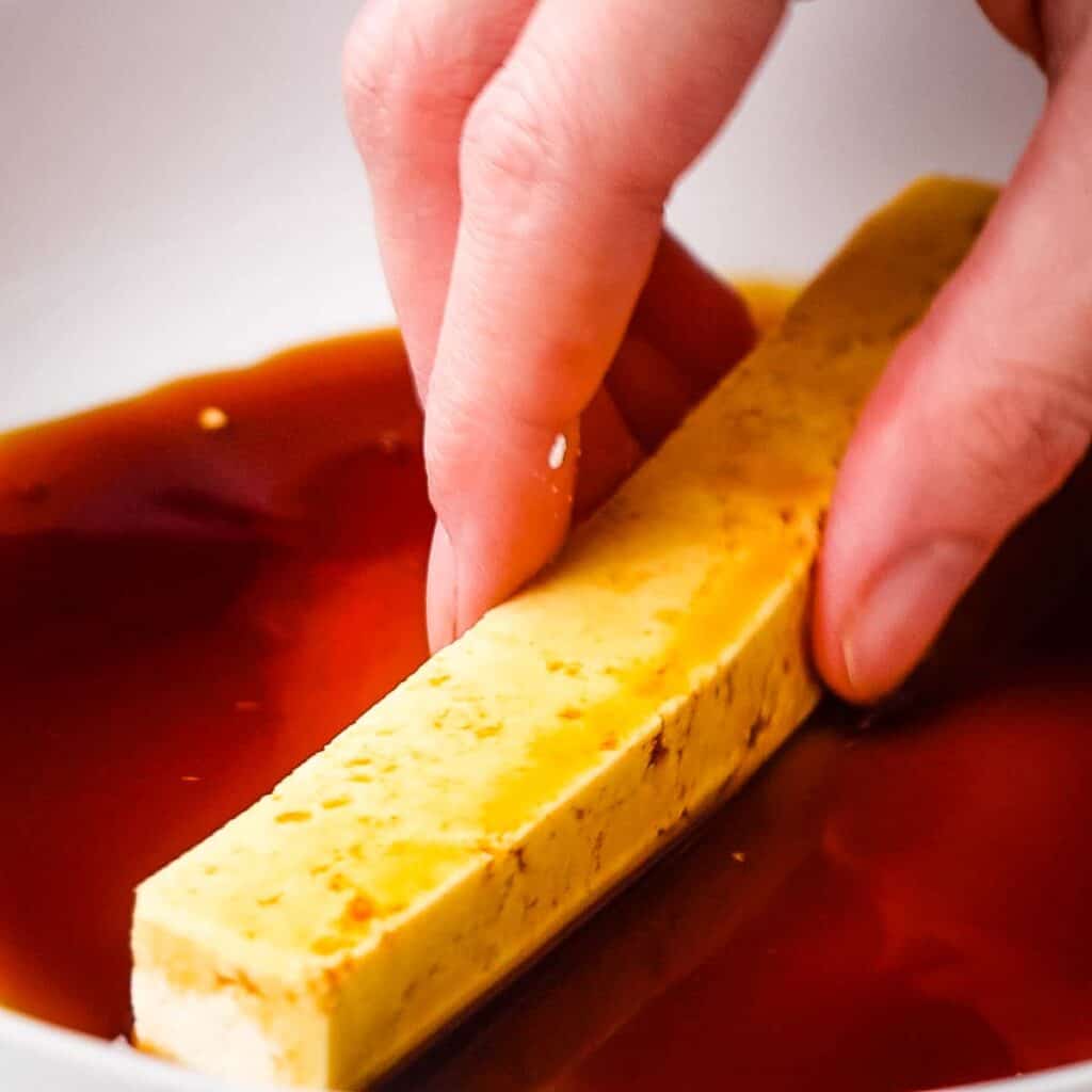 Dipping tofu stick into the tamari.