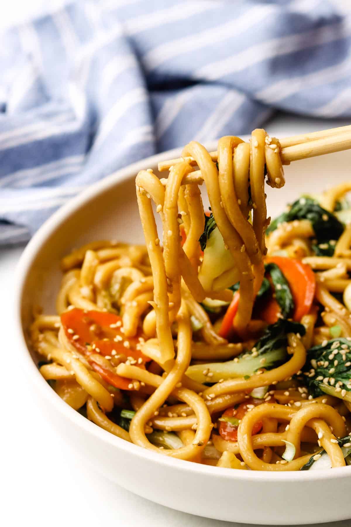 A bowl of Udon stir fry with noodles being eat with chopsticks.