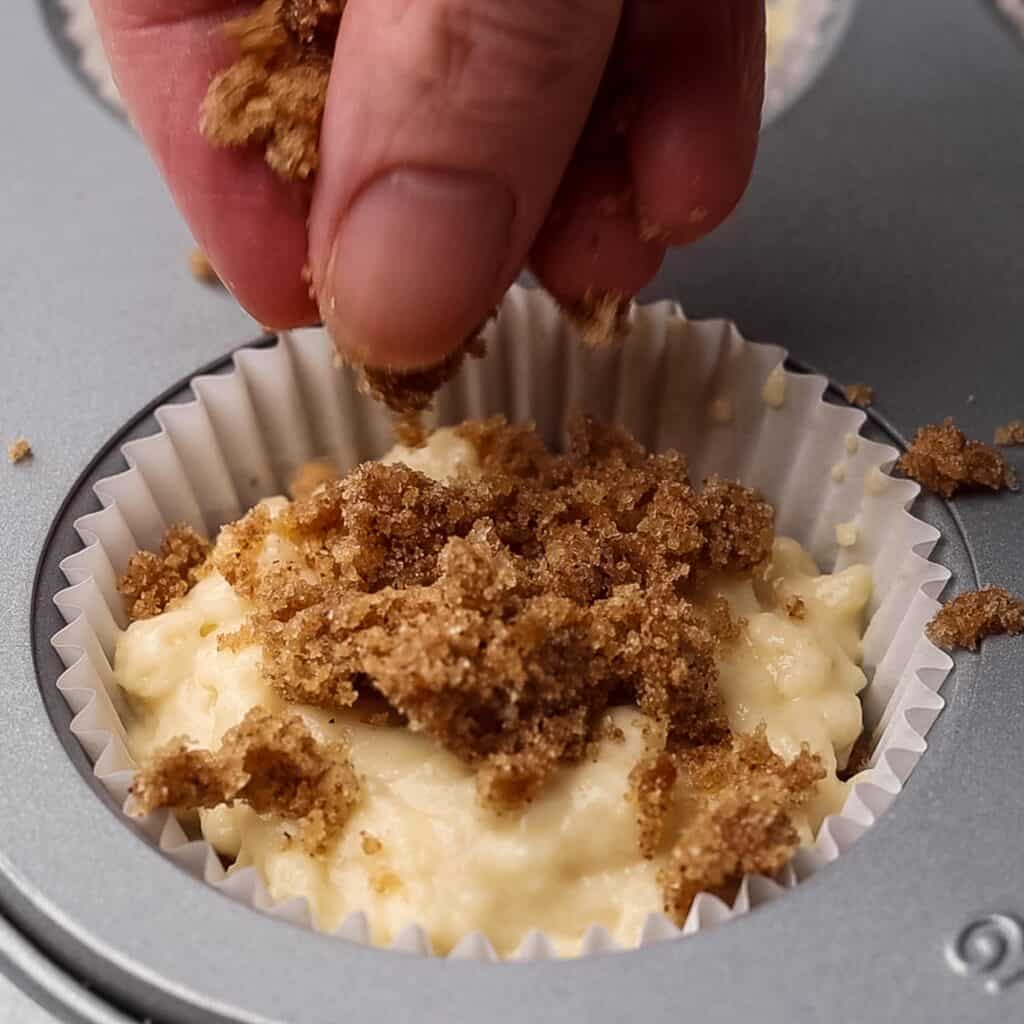 A sprinkle of cinnamon topping being added to the tops of muffins.