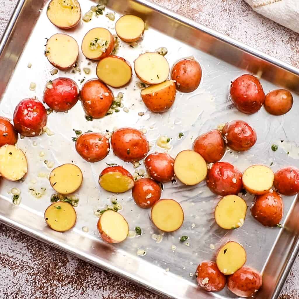 Potatoes placed on a sheet pan with seasoning on top.