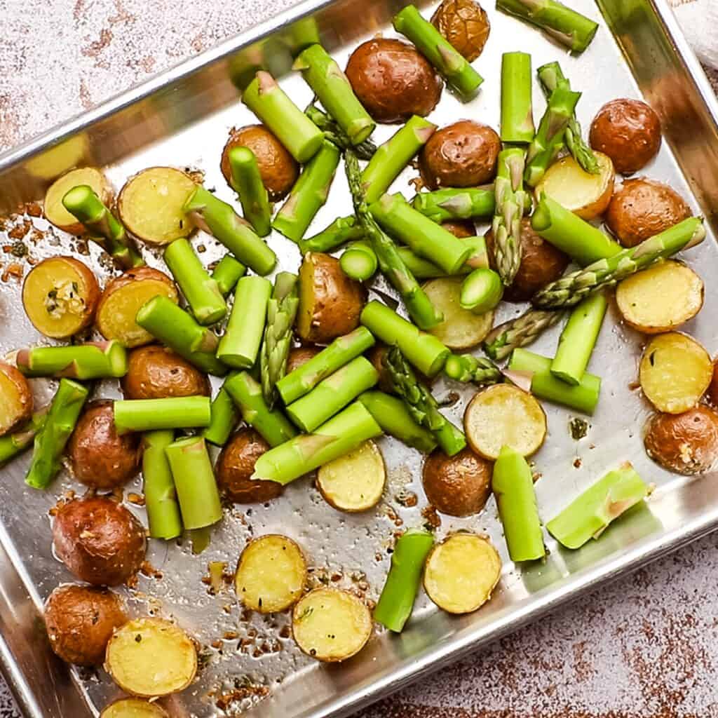 Fresh asparagus added to roasted potatoes on a sheet pan.