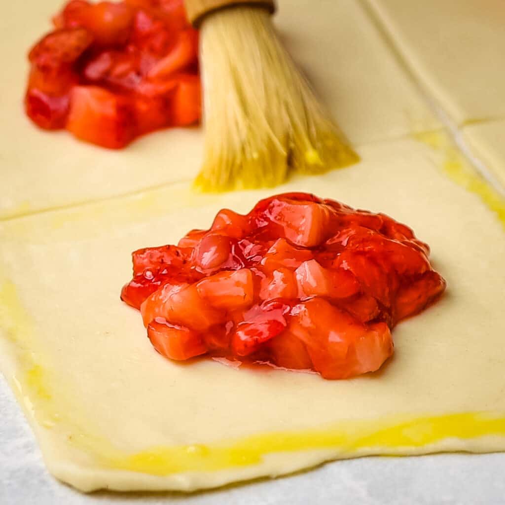 Brushing egg wash on puff pastry with strawberry filling.