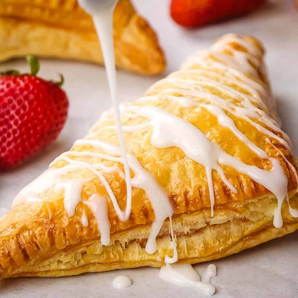 Vanilla icing drizzled on a strawberry turnover.