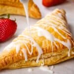A strawberry turnover being drizzled with vanilla glaze.