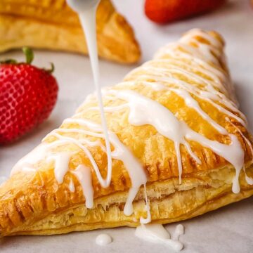 A strawberry turnover being drizzled with vanilla glaze.