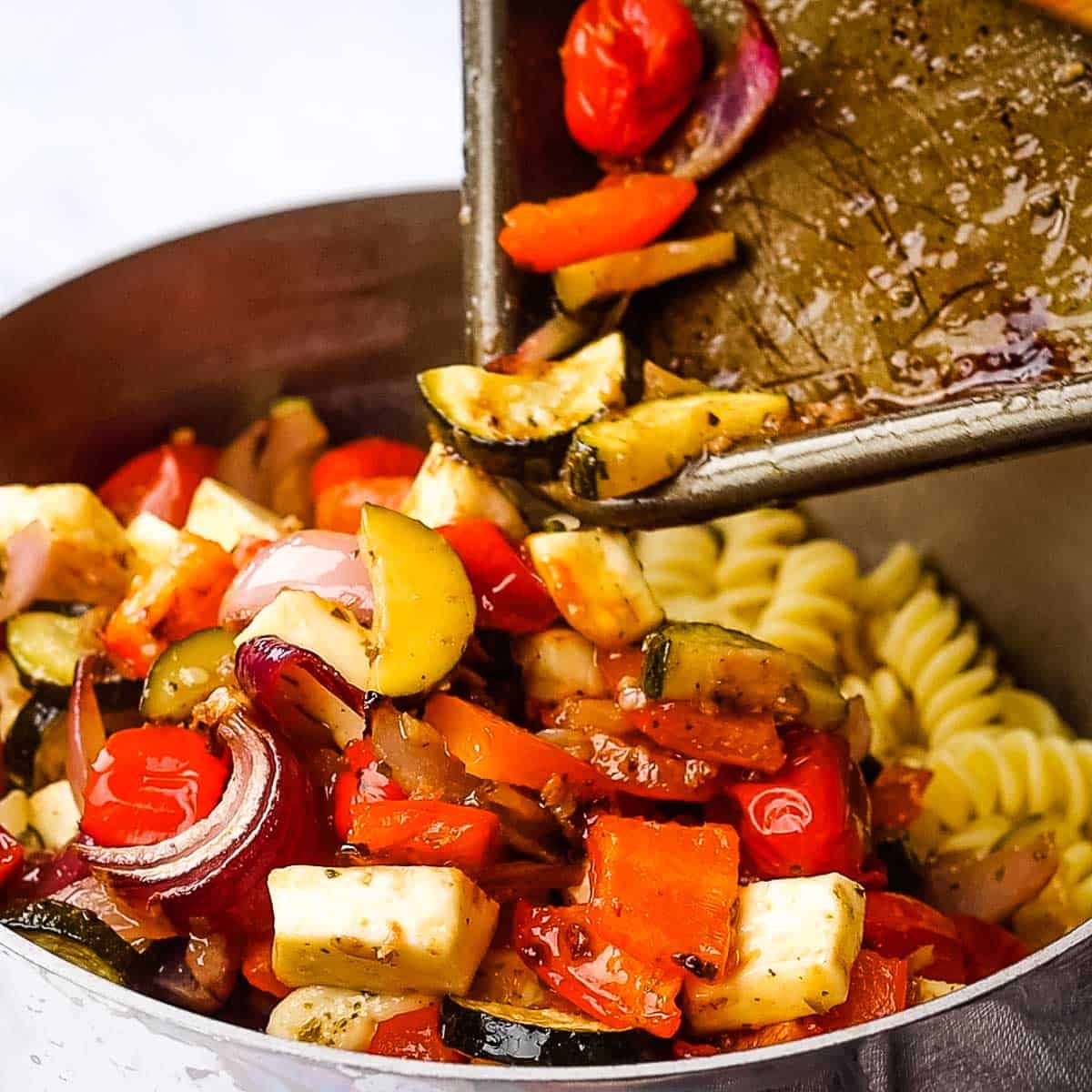 roasted vegetables being added to drained pasta.