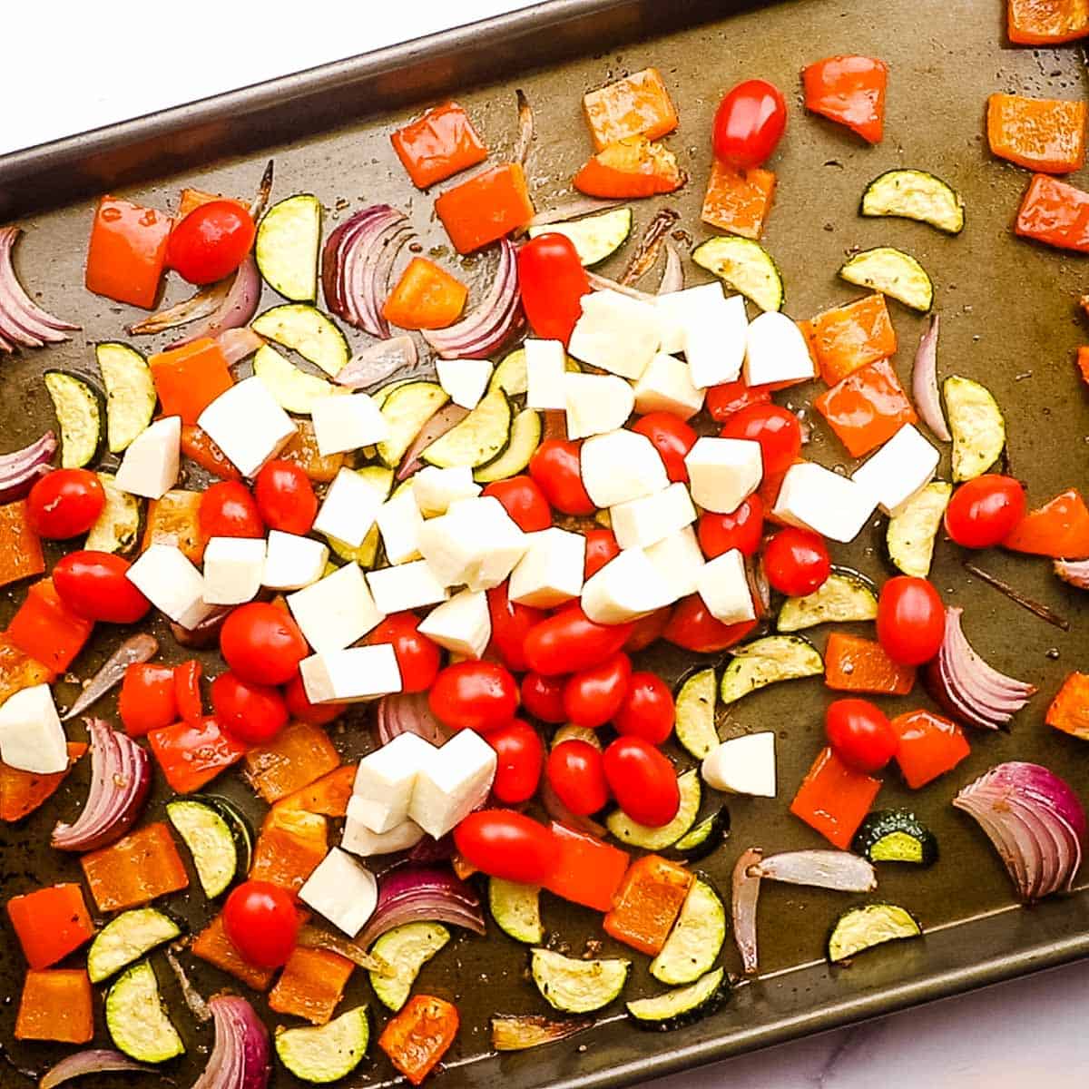 Halloumi cheese and grape tomatoes on a baking sheet with roasted vegetables.