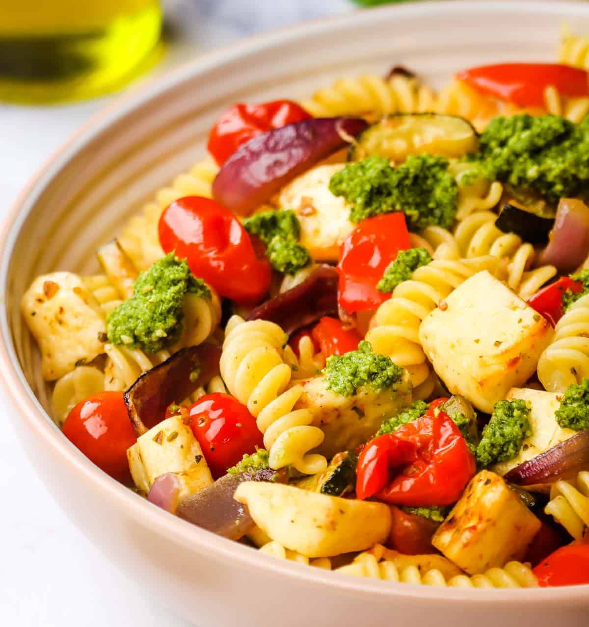 A bowl of halloumi pasta garnished with pesto