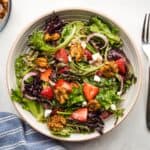 A bowl of strawberry salad with goat cheese and candied walnuts from overhead.