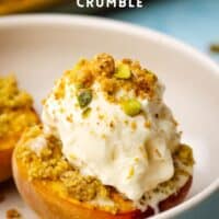 A roasted peach half with a scoop of vanilla ice cream sprinkled with pistachio crumble.