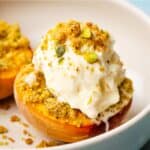 Roasted, halved peaches in a bowl with a scoop of vanilla ice cream and pistachio crumble.
