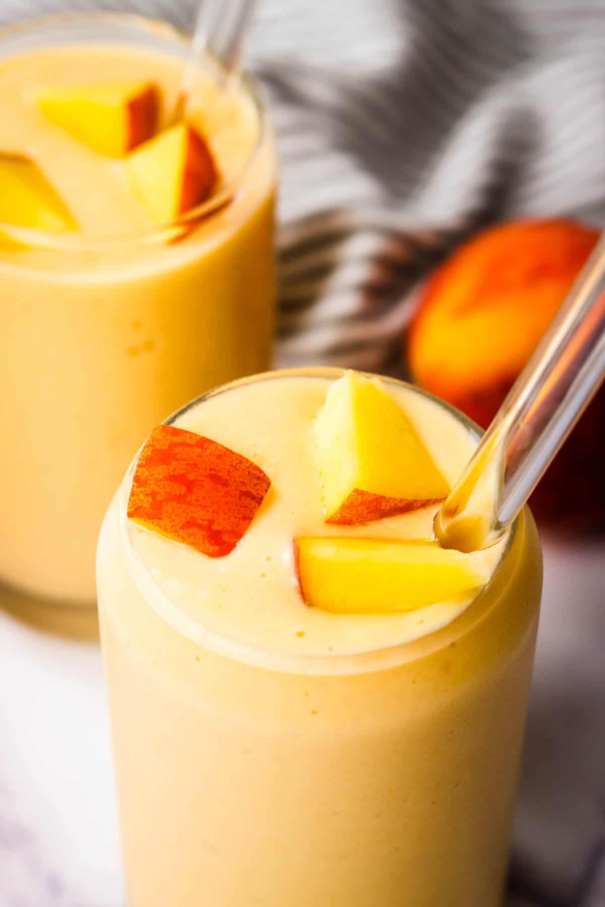 A glass of banana peach smoothie topped with fresh peaches.