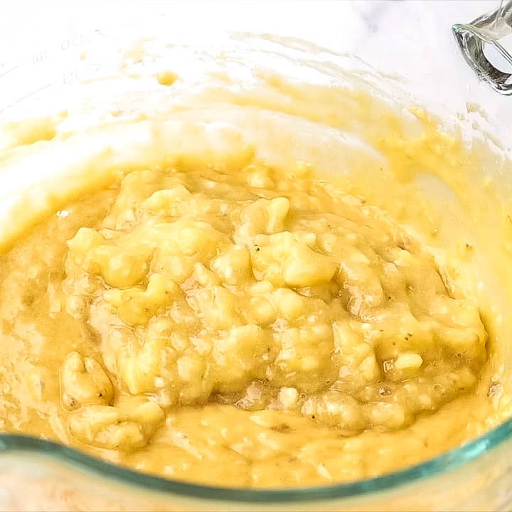close up of banana muffin mixture with mashed bananas on top
