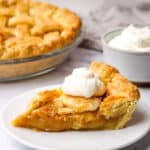 A slice of sugar pie on a plate with a dollop of whipped cream and a whole pie in the background.