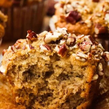 A banana pecan muffin, cut in half to show the inside, sitting on top of a muffin liner.