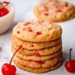 A stack of cherry cookies with maraschino cherries scattered around.