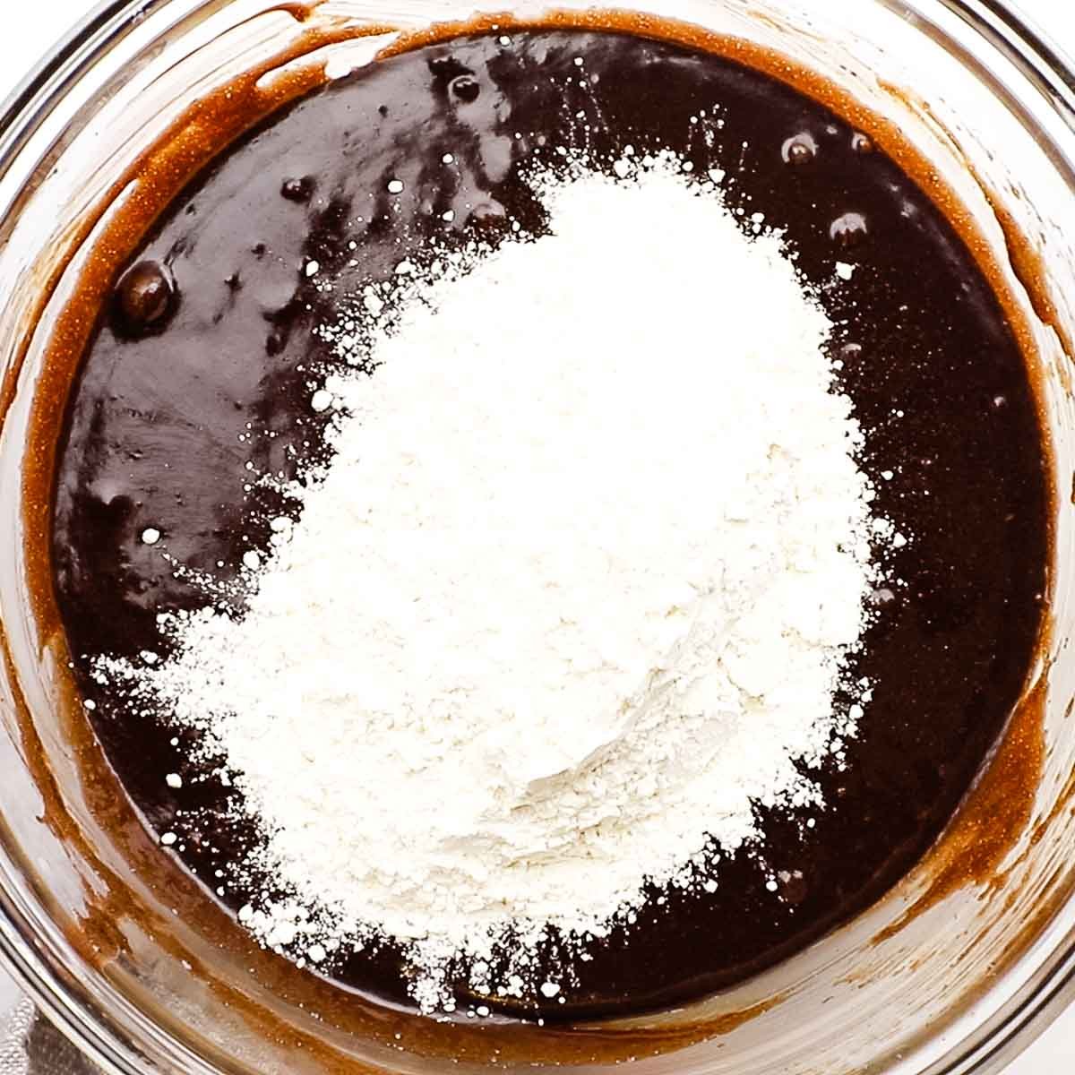 Flour being added to brownie batter in a bowl.