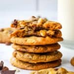 A stack of triple chocolate chip cookies with one halved to show the inside. Glass of milk in the background.
