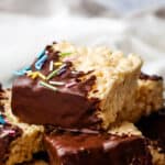 A stack of rice krispie treats half dipped in chocolate and sprinkled with pastel sprinkles.
