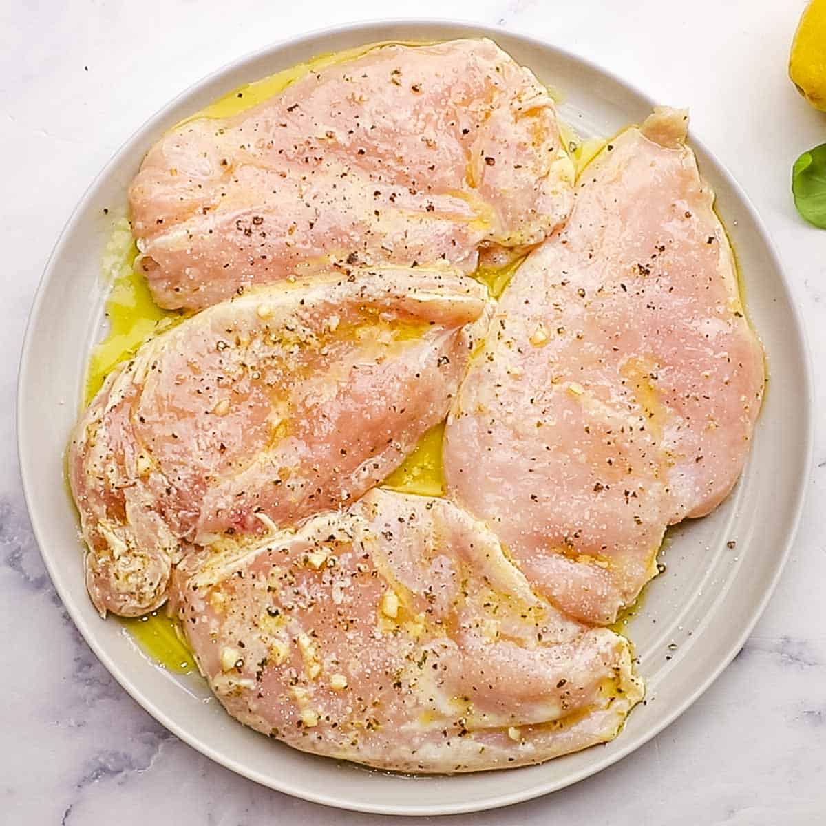 marinated chicken breasts on a plate sprinkled with salt and pepper