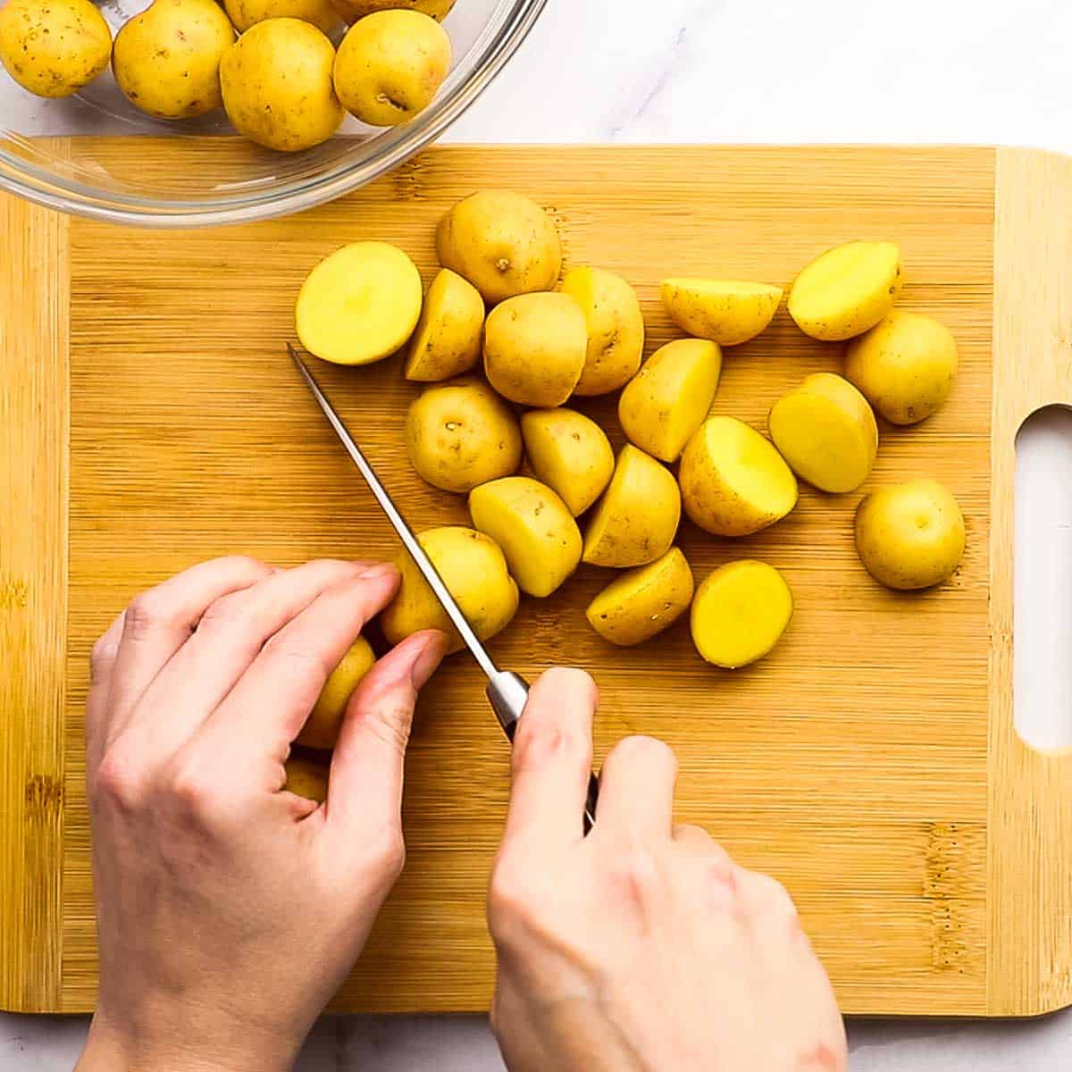 chopping baby potatoes in half on a cutting board
