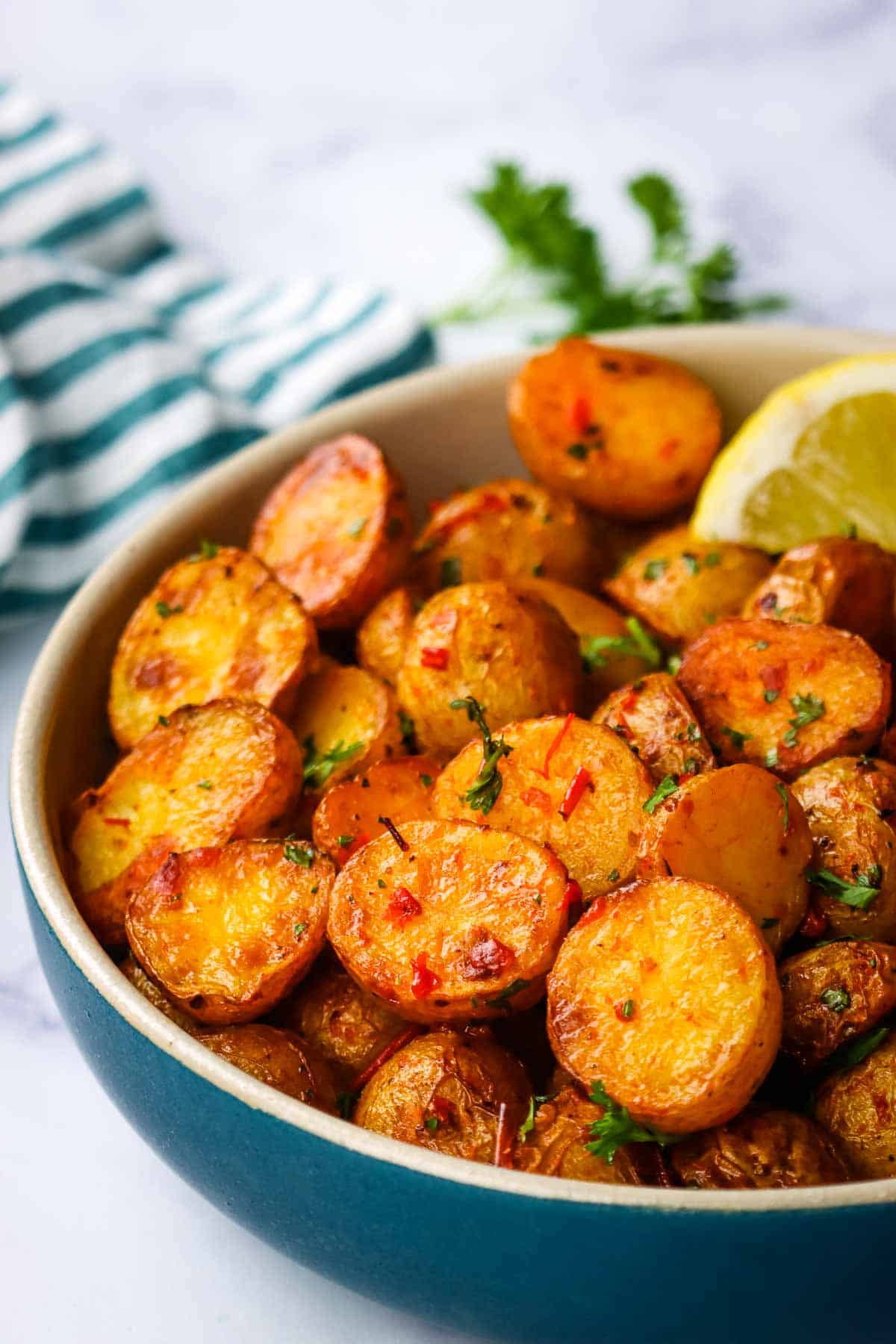 A bowl of roasted harissa potatoes garnished with parsley and a lemon wedge.