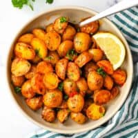 A bowl of roasted harissa potatoes garnished with parsley and a lemon wedge.