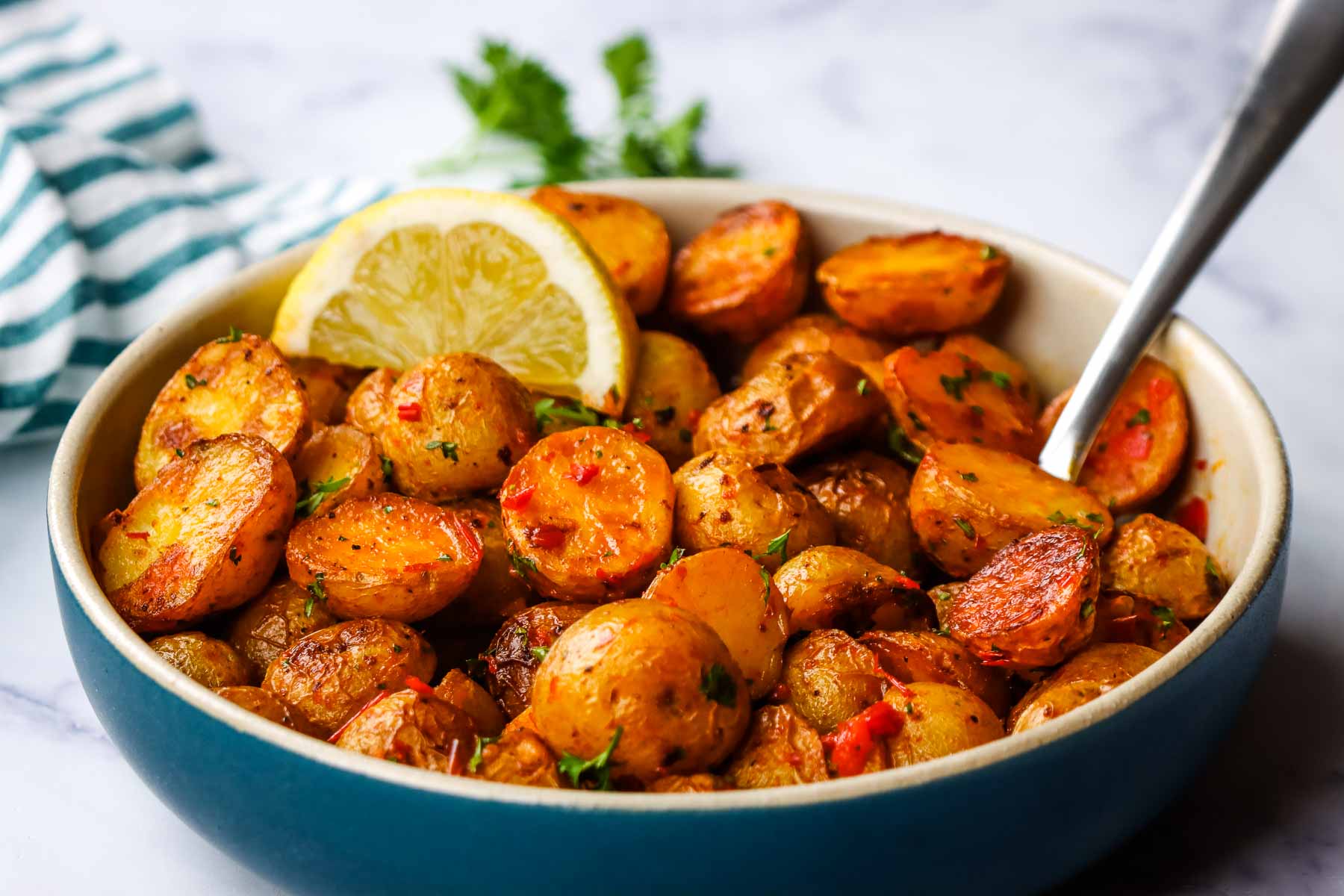 A bowl of roasted harissa potatoes garnished with a lemon wedge.