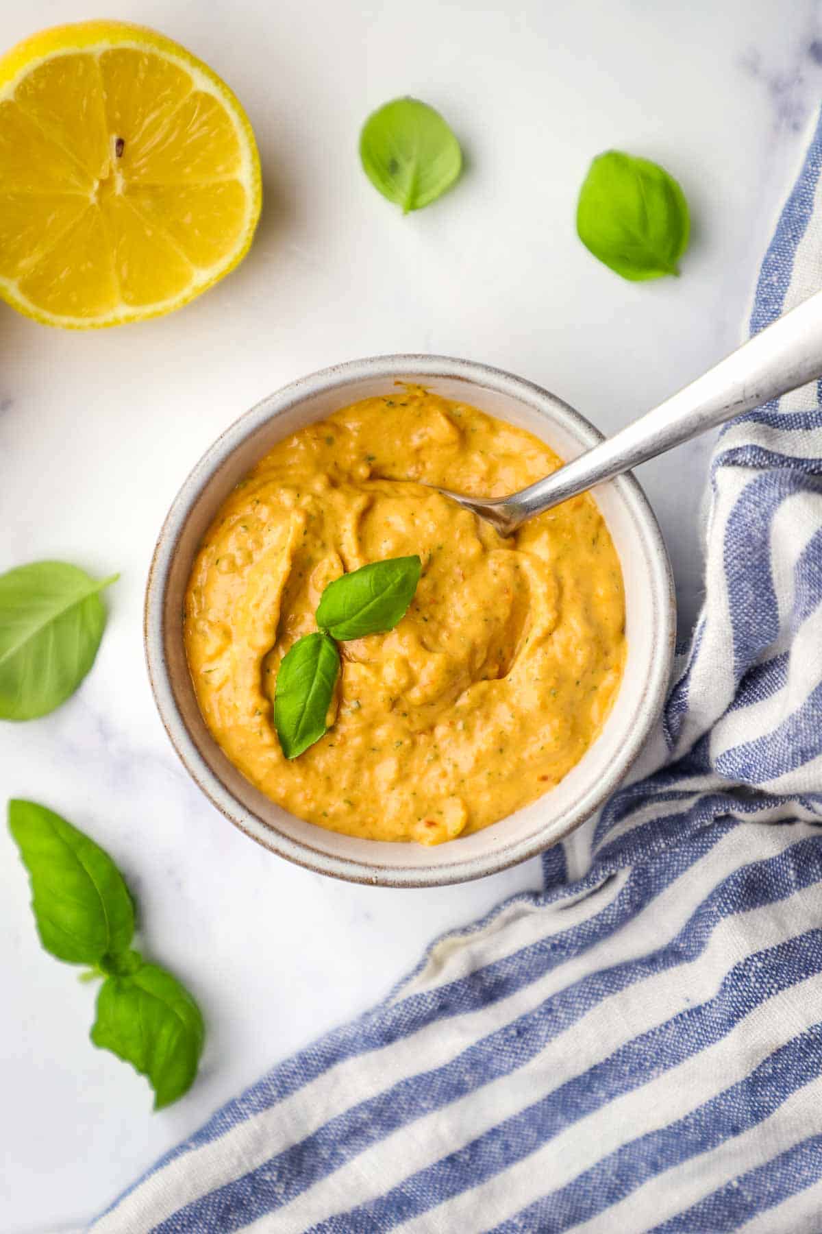 Overhead view of a bowl of sun dried tomato aioli garnished with fresh basil leaves.