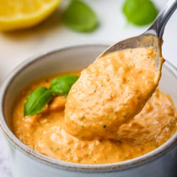 A small bowl of sun dried tomato aioli garnished with basil with a spoonful being scooped out.