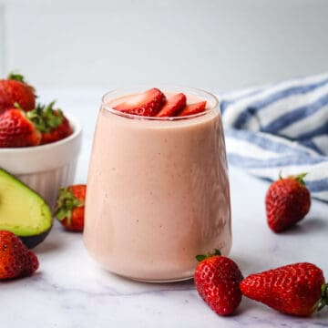 A strawberry avocado smoothie in a glass garnished with strawberries.