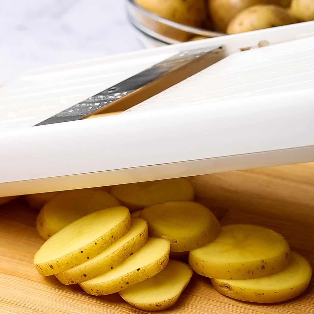 slicing potatoes with a slicer on a cutting board