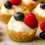 A closeup of a no-bake mini lemon cheesecake tart garnished with a blueberry and a raspberry.