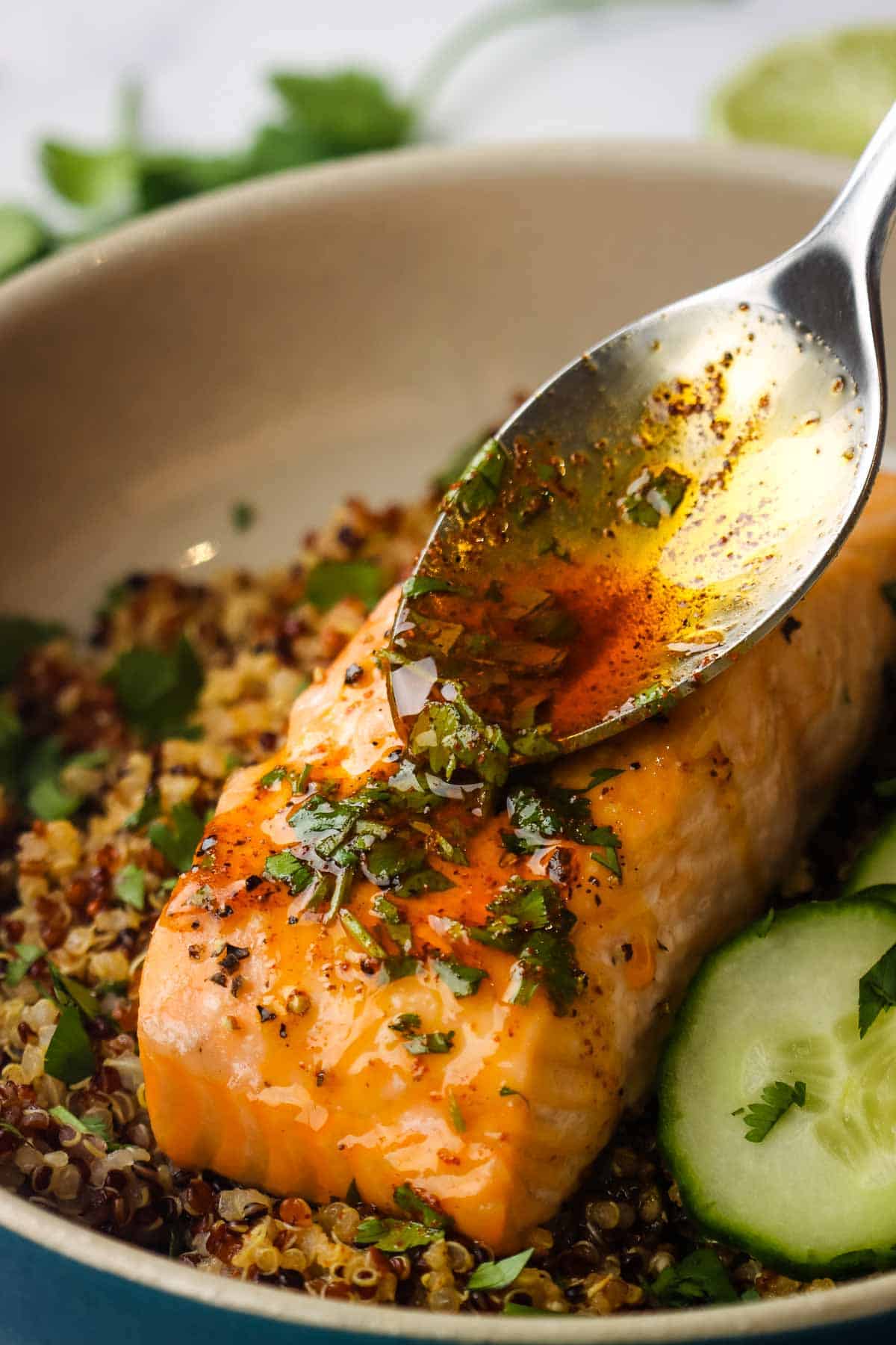 A roasted salmon filet on a bed of quinoa being drizzled with dressing with a spoon.