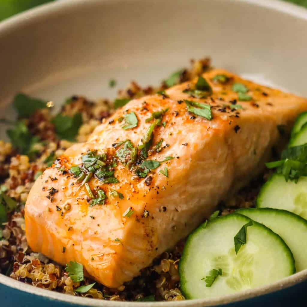 Closeup of a roasted salmon fillet on a bed of quinoa garnished with cucumber and cilantro.
