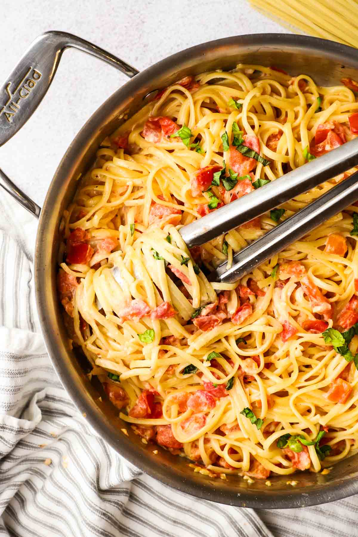 A pan of tomato Alfredo linguine twirled around a pair of tongs.