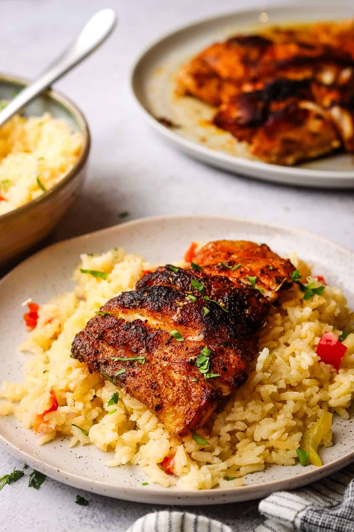 A side view of a plate of balckened fish on a bed of vegetable rice.