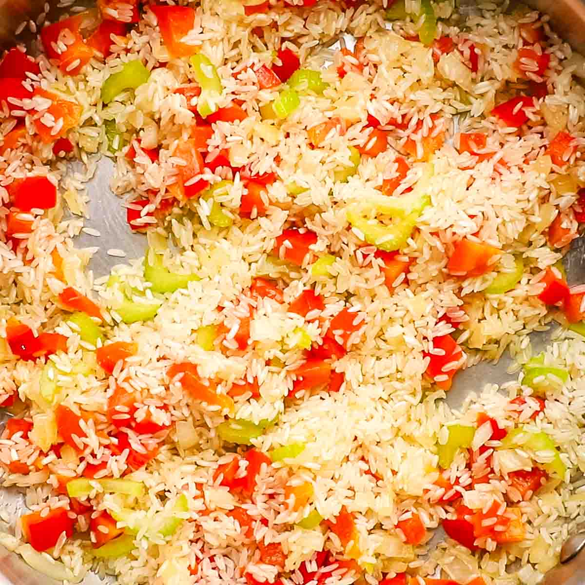 A pan of uncooked rice mixed into cooked vegetables.